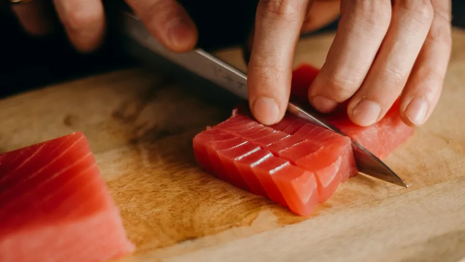 Hands slicing tuna on a wooden board.