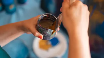 Hände halten Pinsel und Glas auf Tisch.