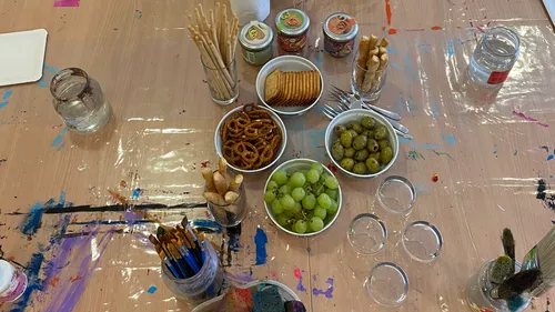 Snacks und Kunstzubehör auf einem unordentlichen Tisch.