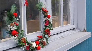 Festive wreath hanging beside a window outdoors.
