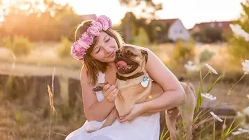 Woman hugs dog outdoors in sunny field.
