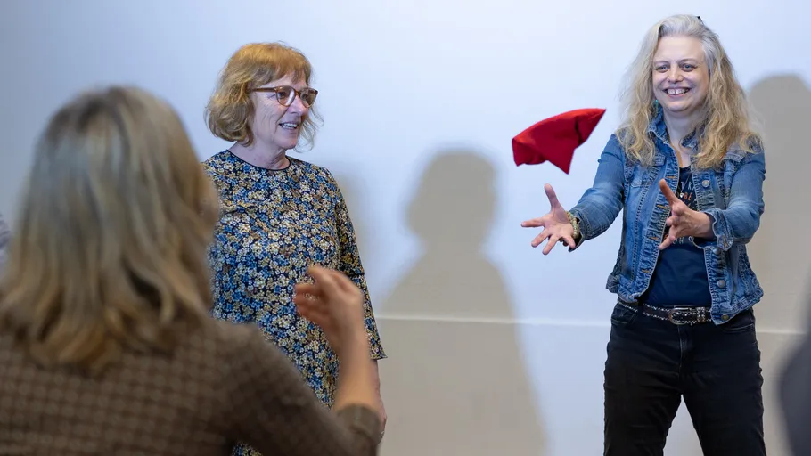 Women in a room tossing a red cloth.