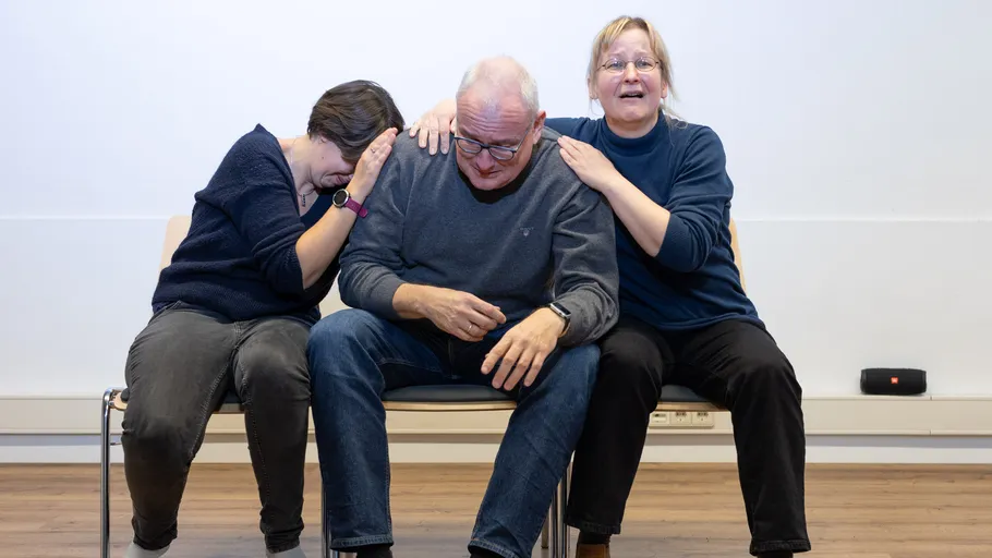 Three people sitting closely on chairs indoors.