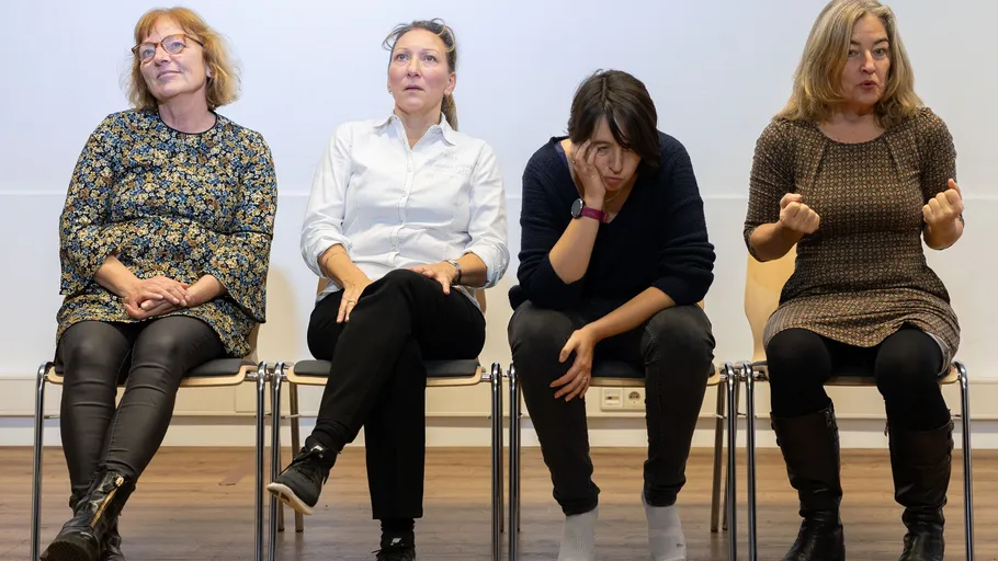 Four women seated on chairs expressing different emotions.