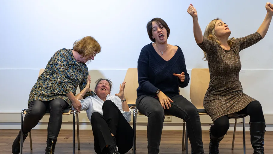 Four women acting out emotions on chairs.