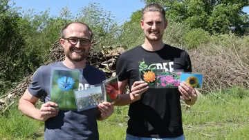 Zwei Männer halten Blumenbilder im Freien.