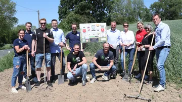Gruppe hält Gartengeräte auf sonnigem Feld.