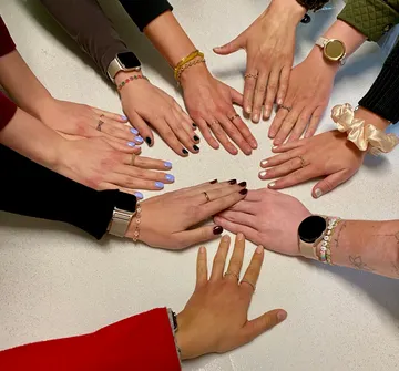 Hände mit Ringen und Armbändern auf Tisch.