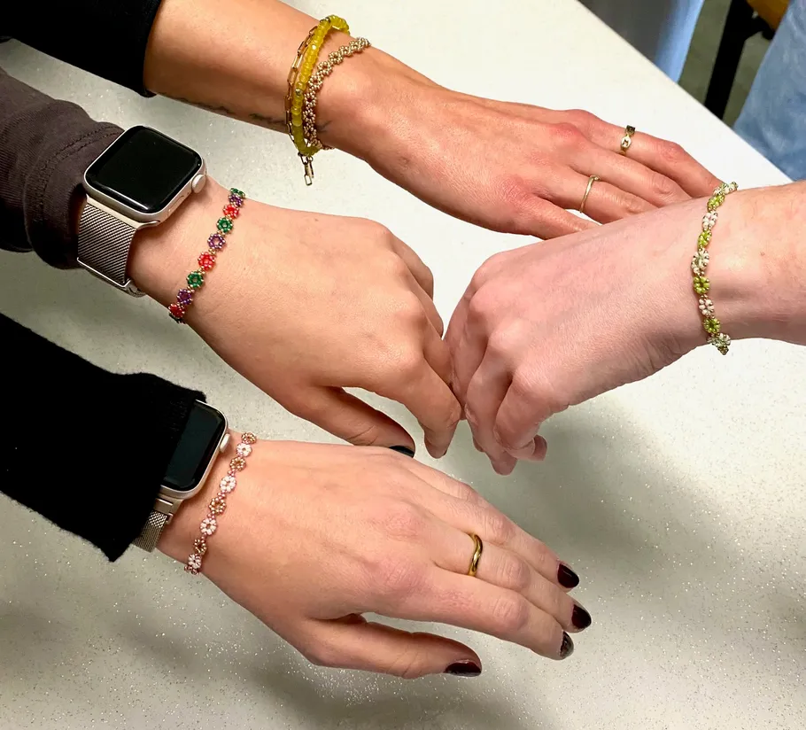 Four hands displaying colorful bead bracelets.