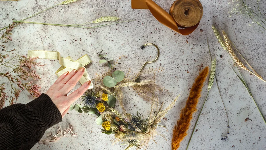 Hand bastelt Kranz mit Trockenblumen.