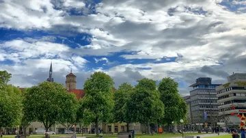 Trees and buildings under a cloudy sky.
