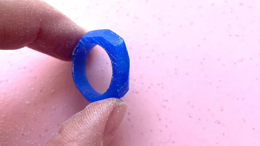 Hand holding blue ring on pink surface.