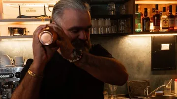 Bartender shaking cocktail shaker at dimly lit bar.
