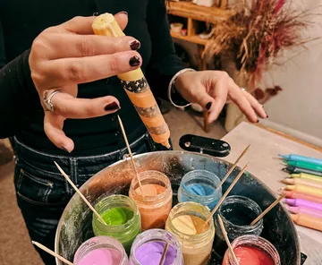 Hands dipping candle into colorful wax jars.