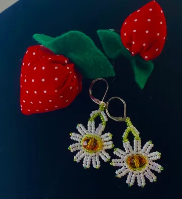 Beaded daisy earrings on dark surface.