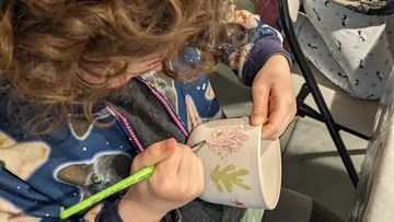 Kind bemalt Keramik drinnen mit einem Stift.