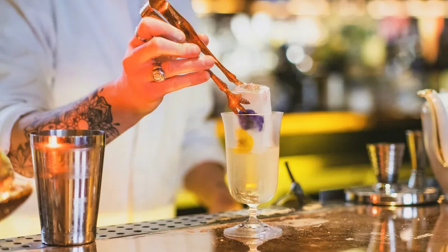 Bartender placing ice in cocktail glass at bar.