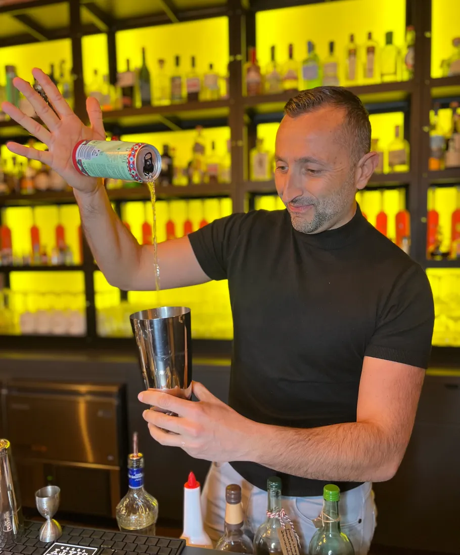 Man pours drink into shaker at a bar.