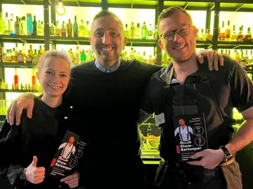 Drei Personen lächeln vor einer Bar.