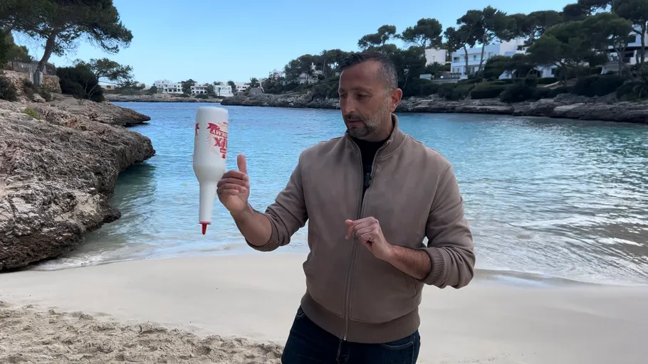 Man balancing sauce bottle on fingers at beach.