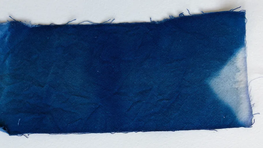 Blue fabric swatch with frayed edges on white surface.