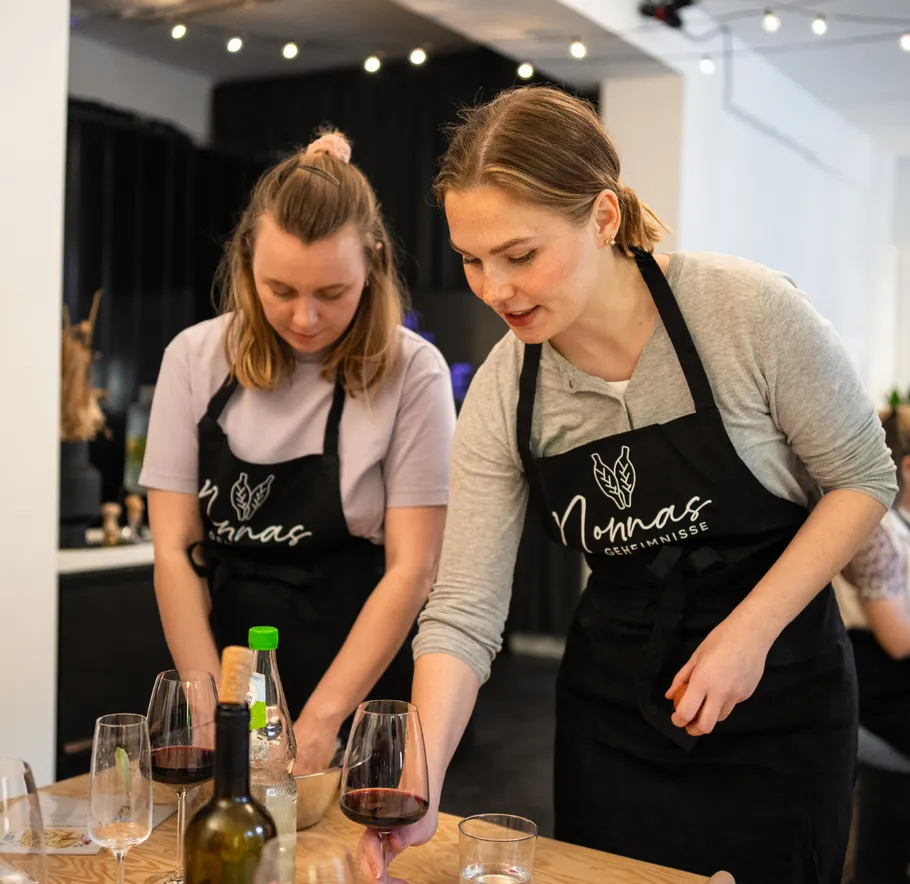 Two women preparing food with wine glasses.