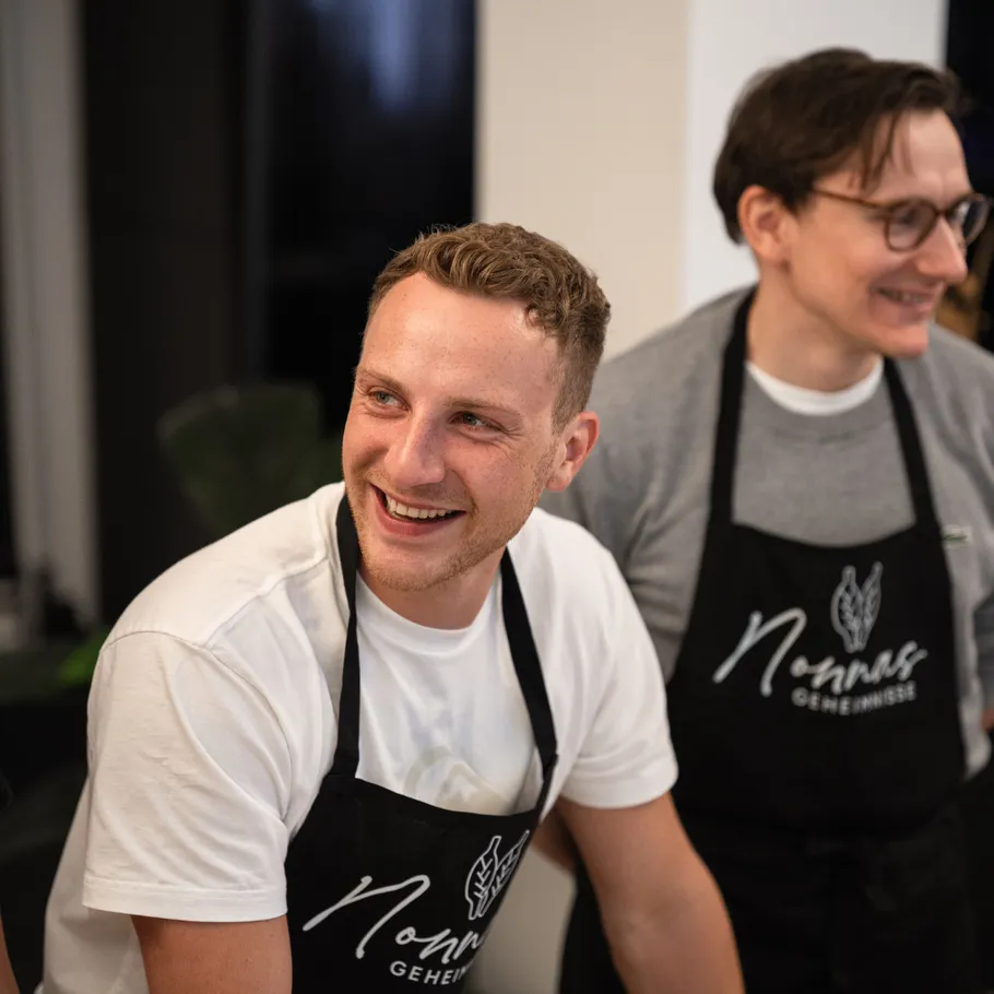 Two smiling men wearing aprons indoors.