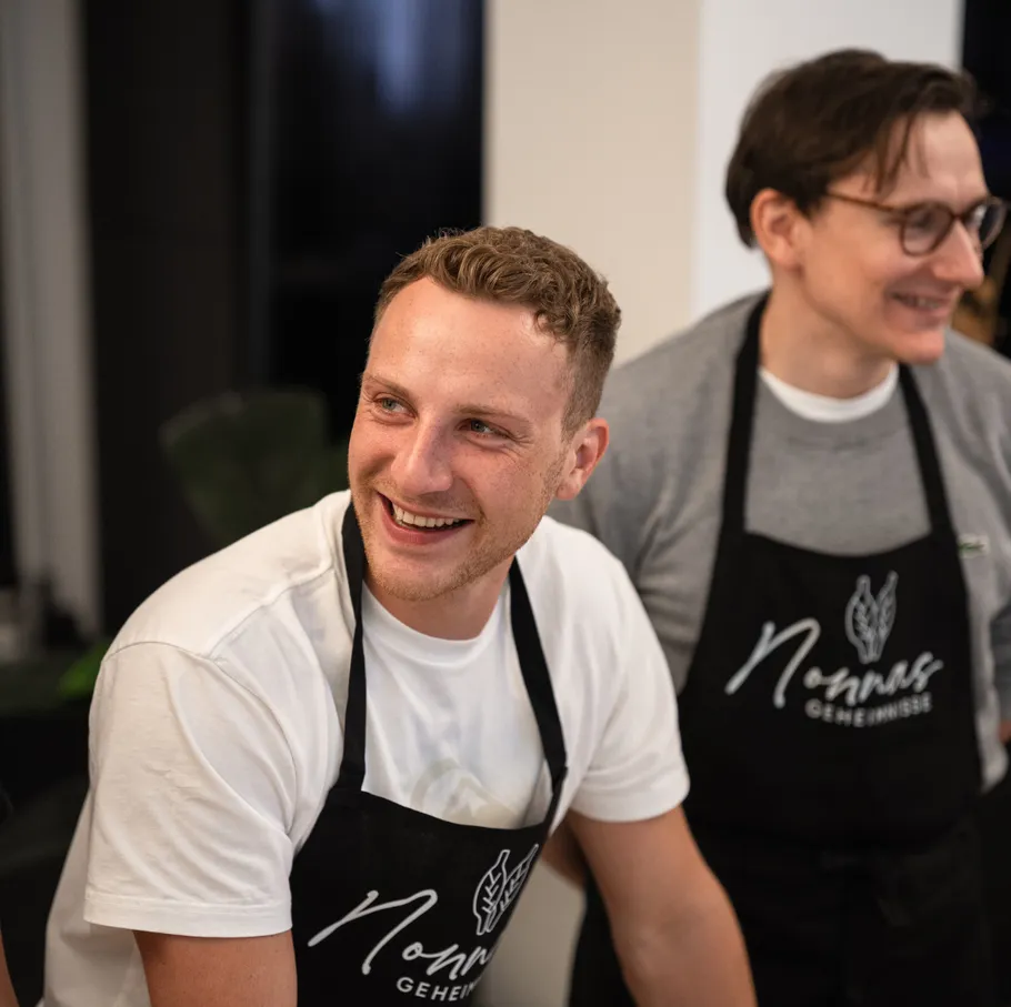 Two people smiling, wearing aprons indoors.