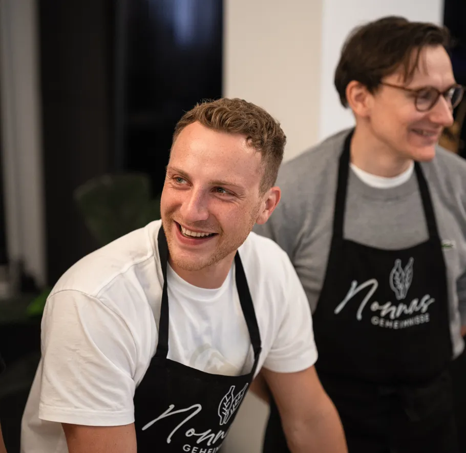 Two men smiling, wearing aprons indoors.