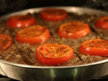 Fleisch mit gebratenen Tomatenscheiben in einer Pfanne.