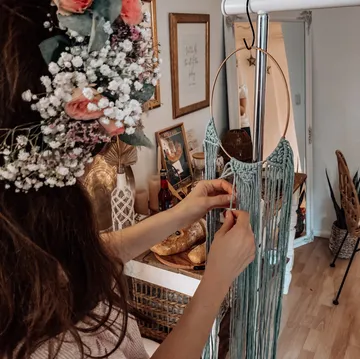 Woman crafting macramé in decorated room.