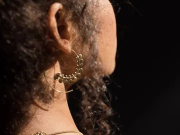 Gold earrings hang on a curly ear in the dark.