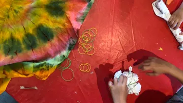 Hände machen Batik auf rotem Tisch.