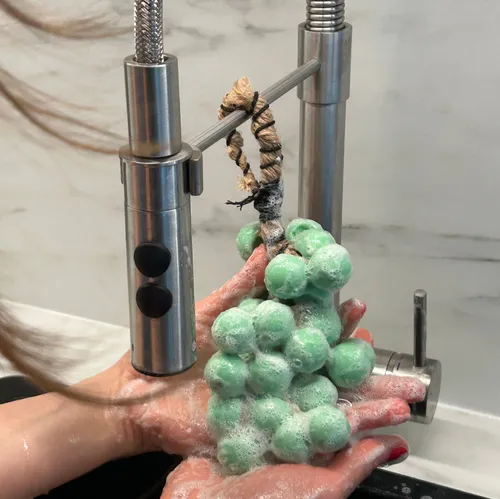 Green grapes soap held under running faucet.