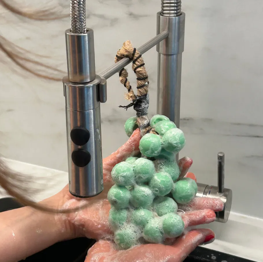 Green grapes soap held under running faucet.