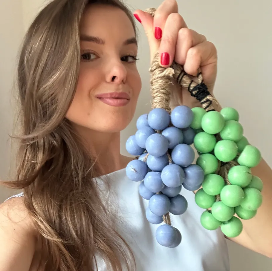 Woman holding decorative grape clusters indoors.