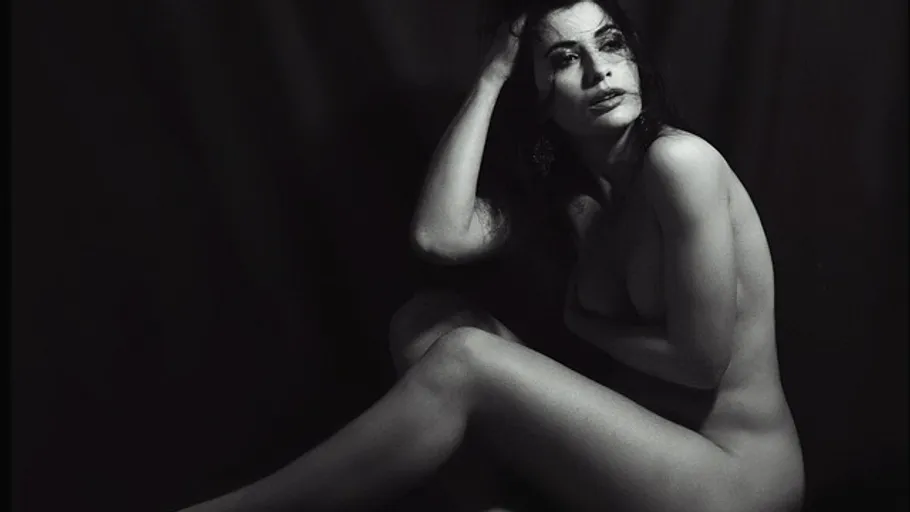 Nude woman posing gracefully against dark background.