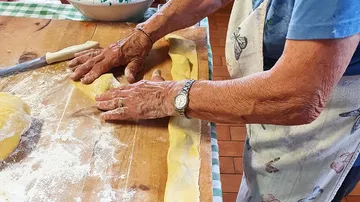 Person macht Pasta an einem Holztisch.
