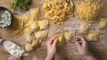 Hands making ravioli on wooden table.