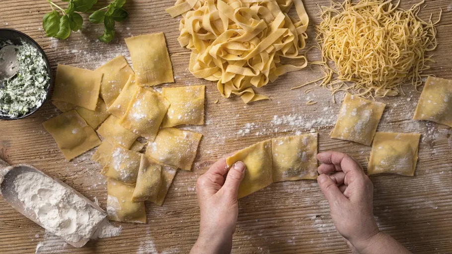 Hands making ravioli on wooden table.