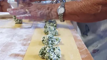 Hände formen Teig mit Spinatfüllung auf Tisch.