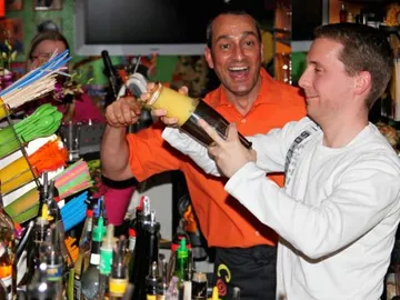 Two men mix cocktails at a colorful bar.