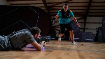 Two men playing laser tag indoors, one crouching.