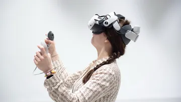 Person wearing VR headset, holding controllers, indoors.