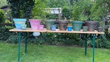 Bunte Töpfe auf Holztisch im Freien ausgestellt.