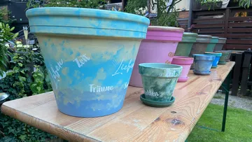 Bunt bemalte Töpfe auf einem Holztisch angeordnet.