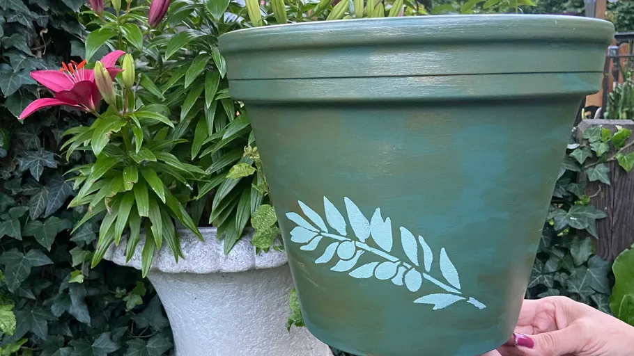 Hand-painted green pot with leaf design outdoors.