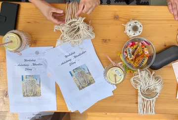 Hände basteln mit Makramee auf Holztisch.