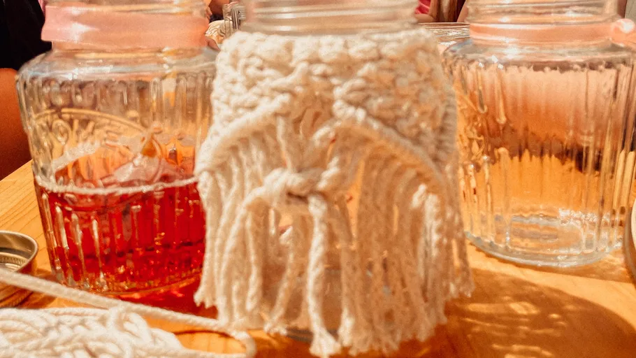 Glass jar with macrame decoration, wooden table.