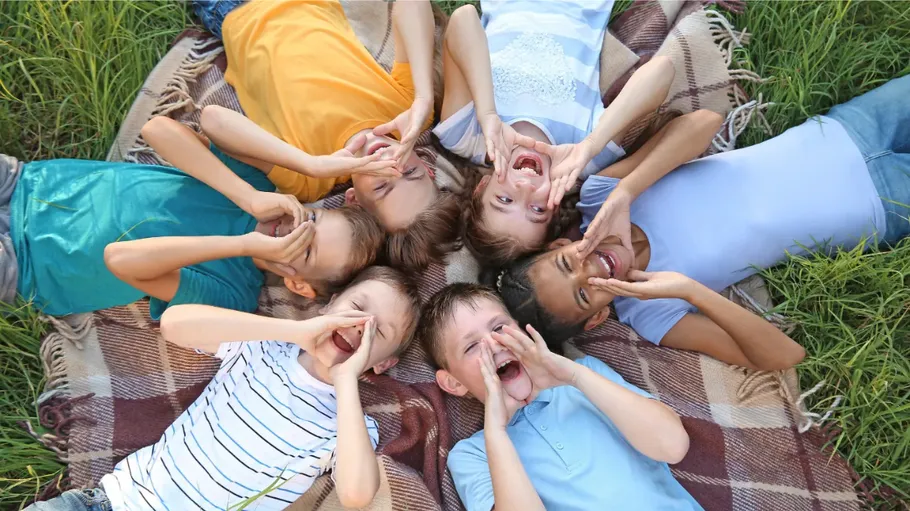 Children lying on blanket, shouting joyfully outside.